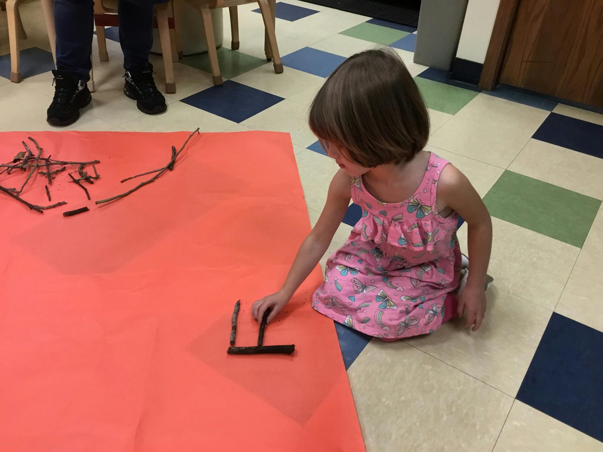 Child kneeling on floor arranging sticks on red paper