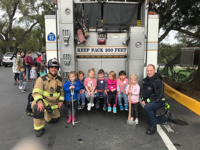 Two firefighters with a group of children in front of a fire truck