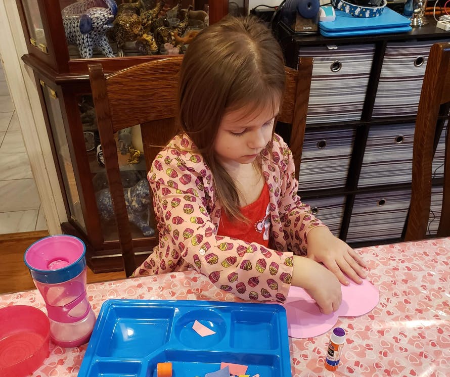 Child sitting at a table doing a craft with pink paper