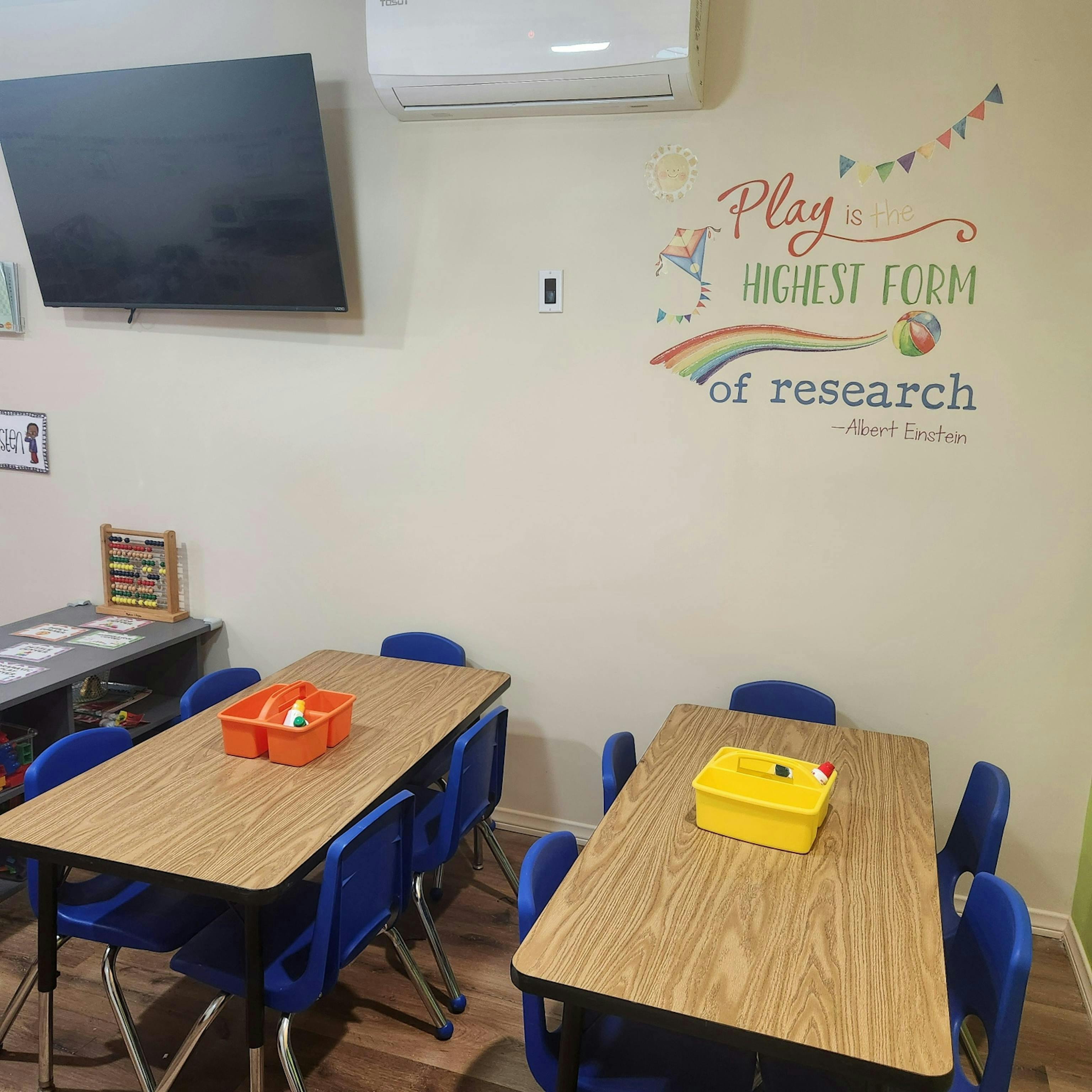Classroom with small tables and chairs, wall art, and a television