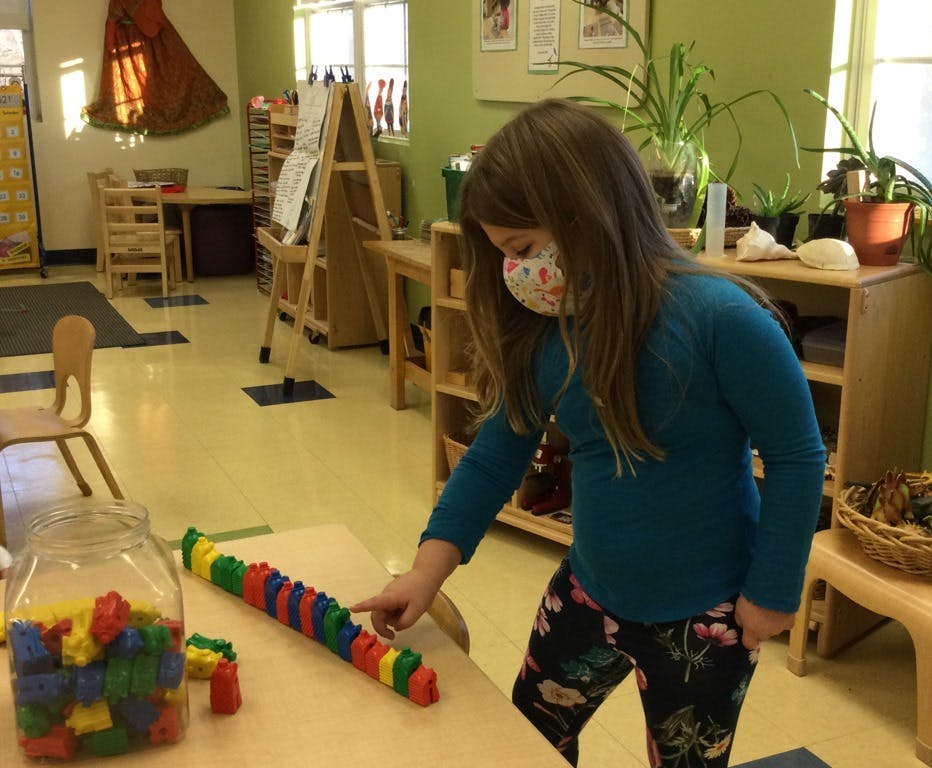 Child in mask playing with colorful interlocking blocks in a classroom