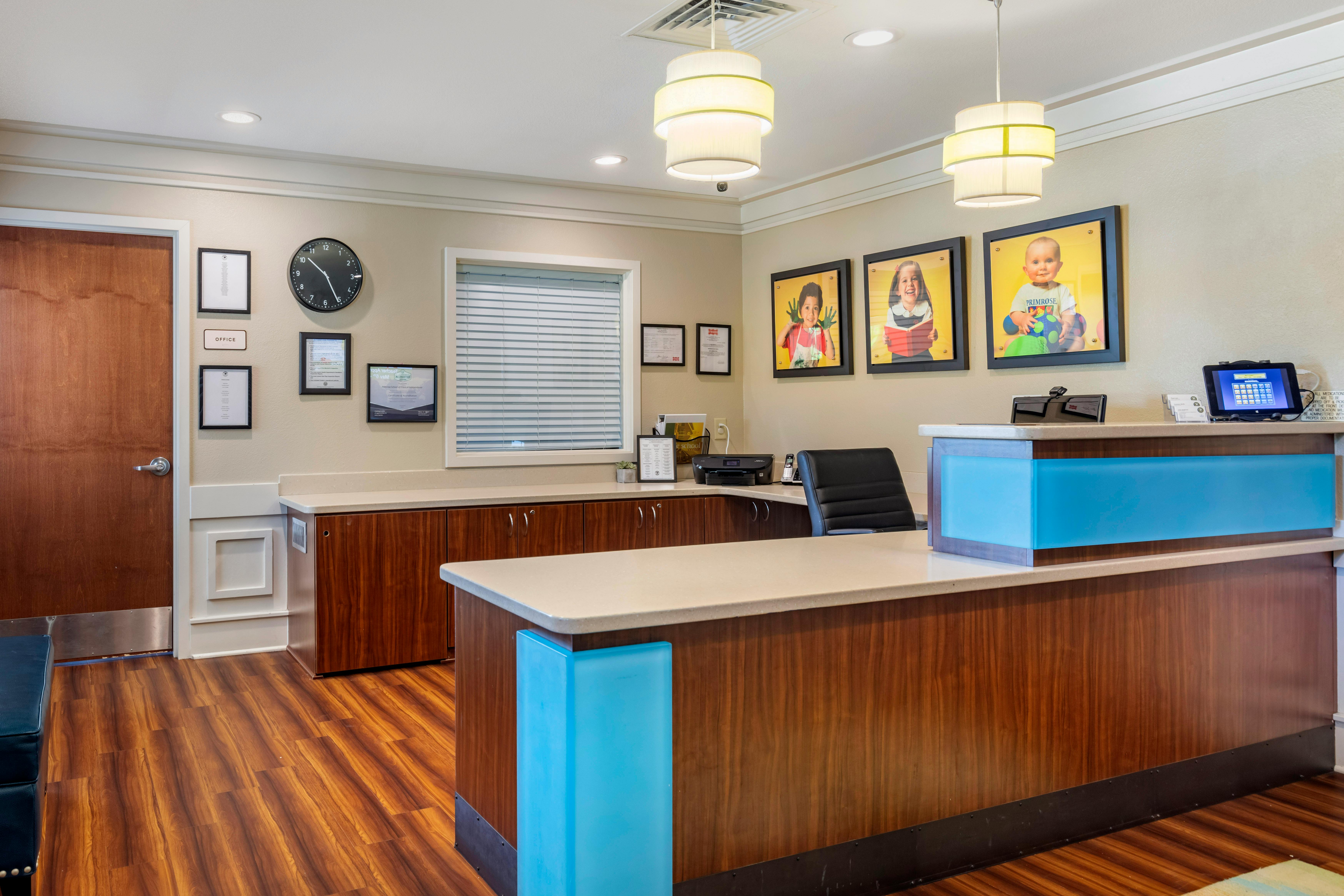 Reception area with a wooden and blue counter, framed child portraits on the wall
