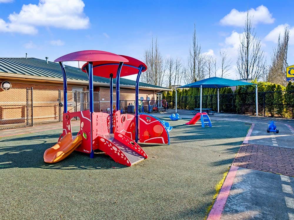 A colorful outdoor playground with red and orange play structures, blue canopy
