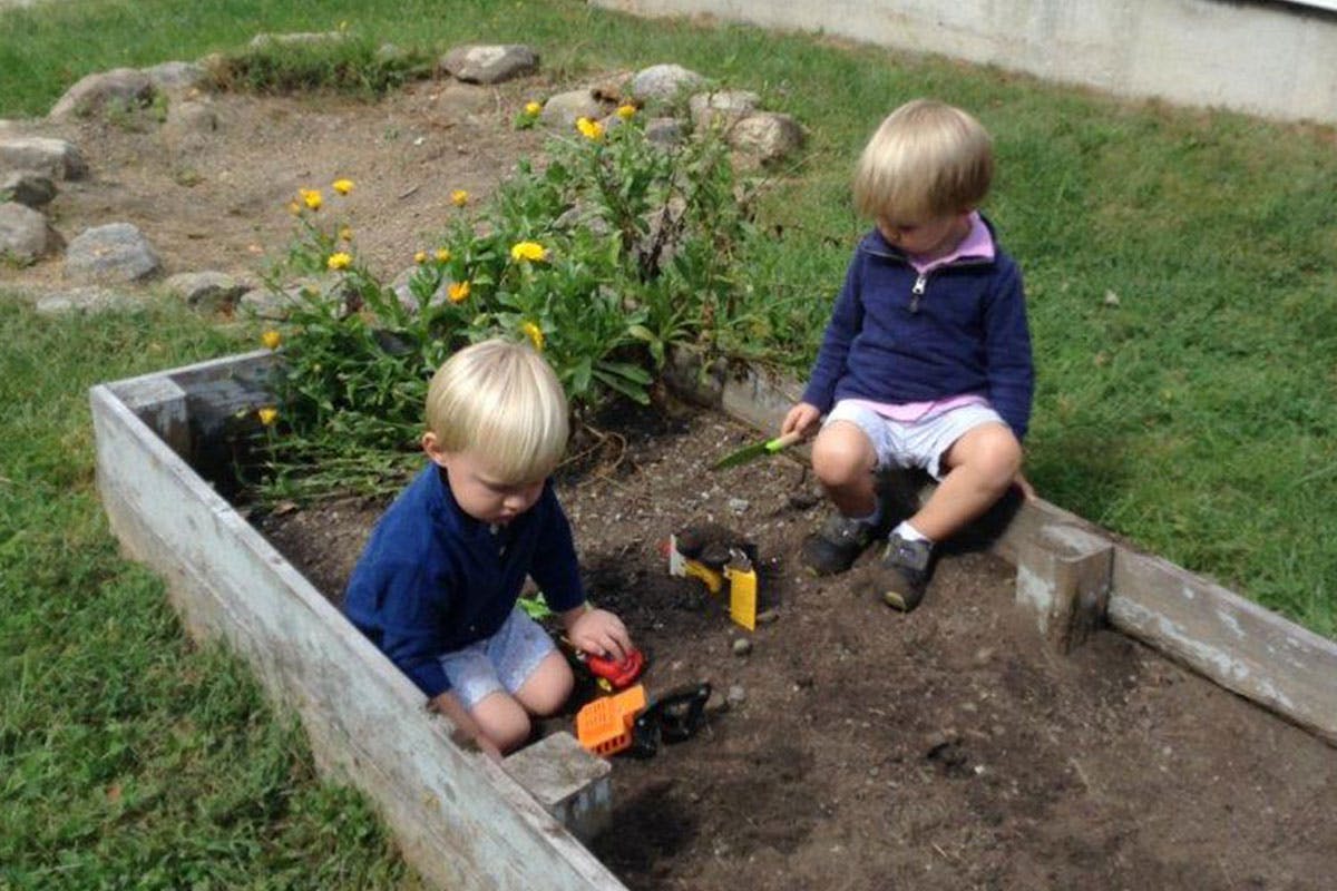 Two children playing with toy trucks in a raised garden bed