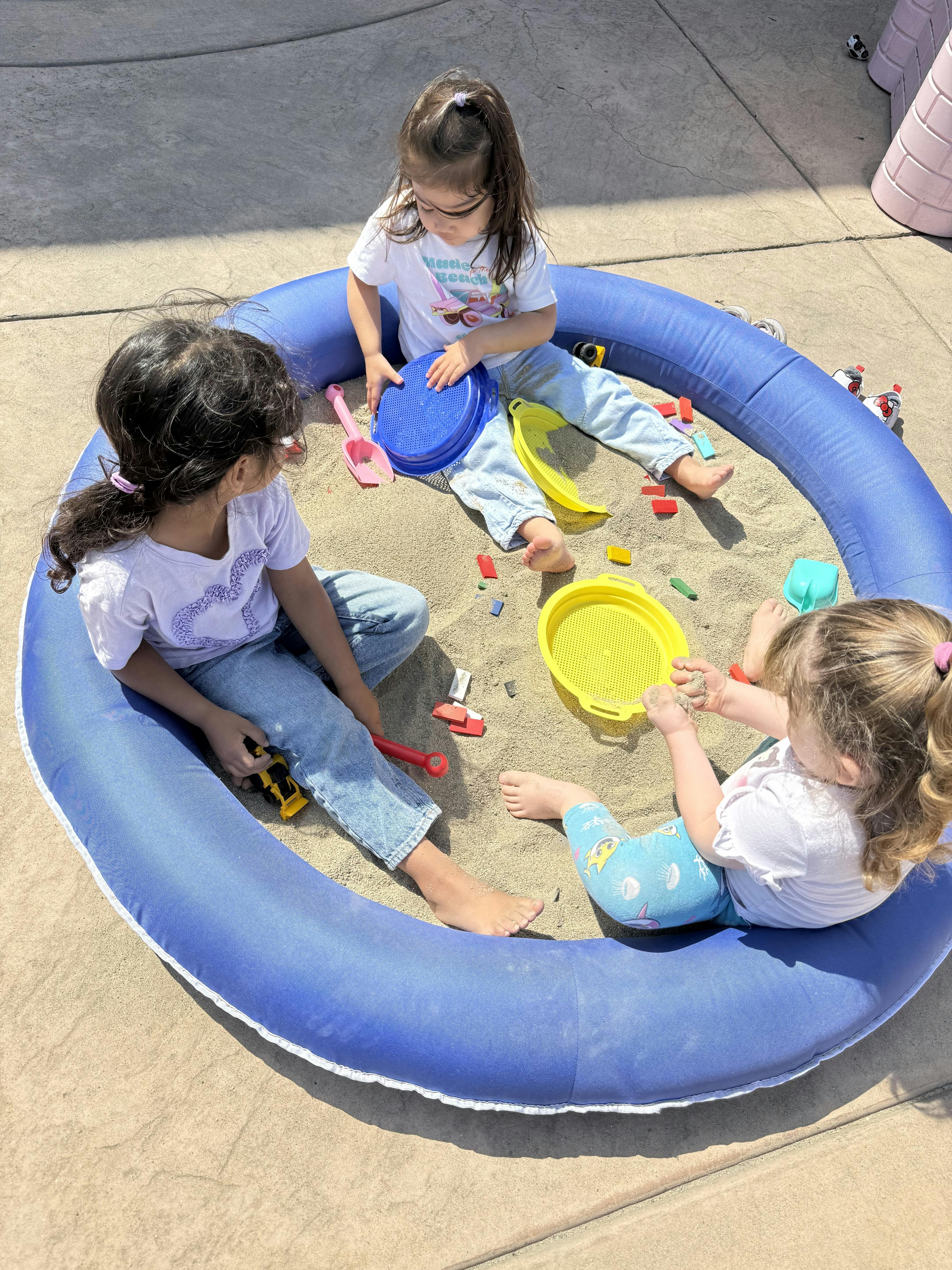 Three children playing in a circular blue sandbox