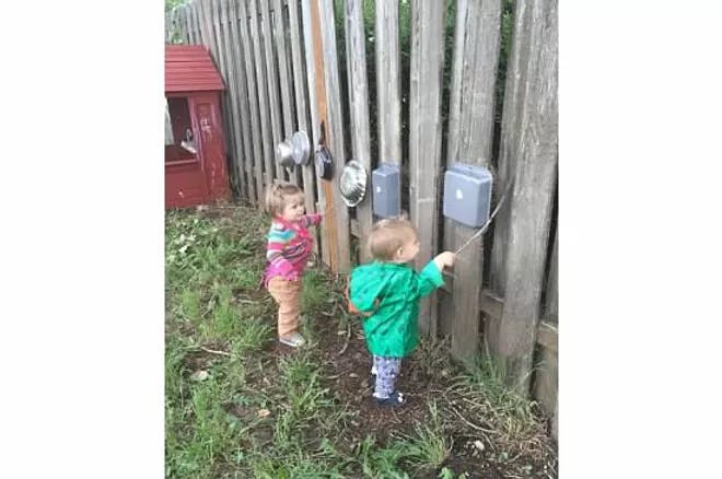 Two children playing with objects attached to a wooden fence
