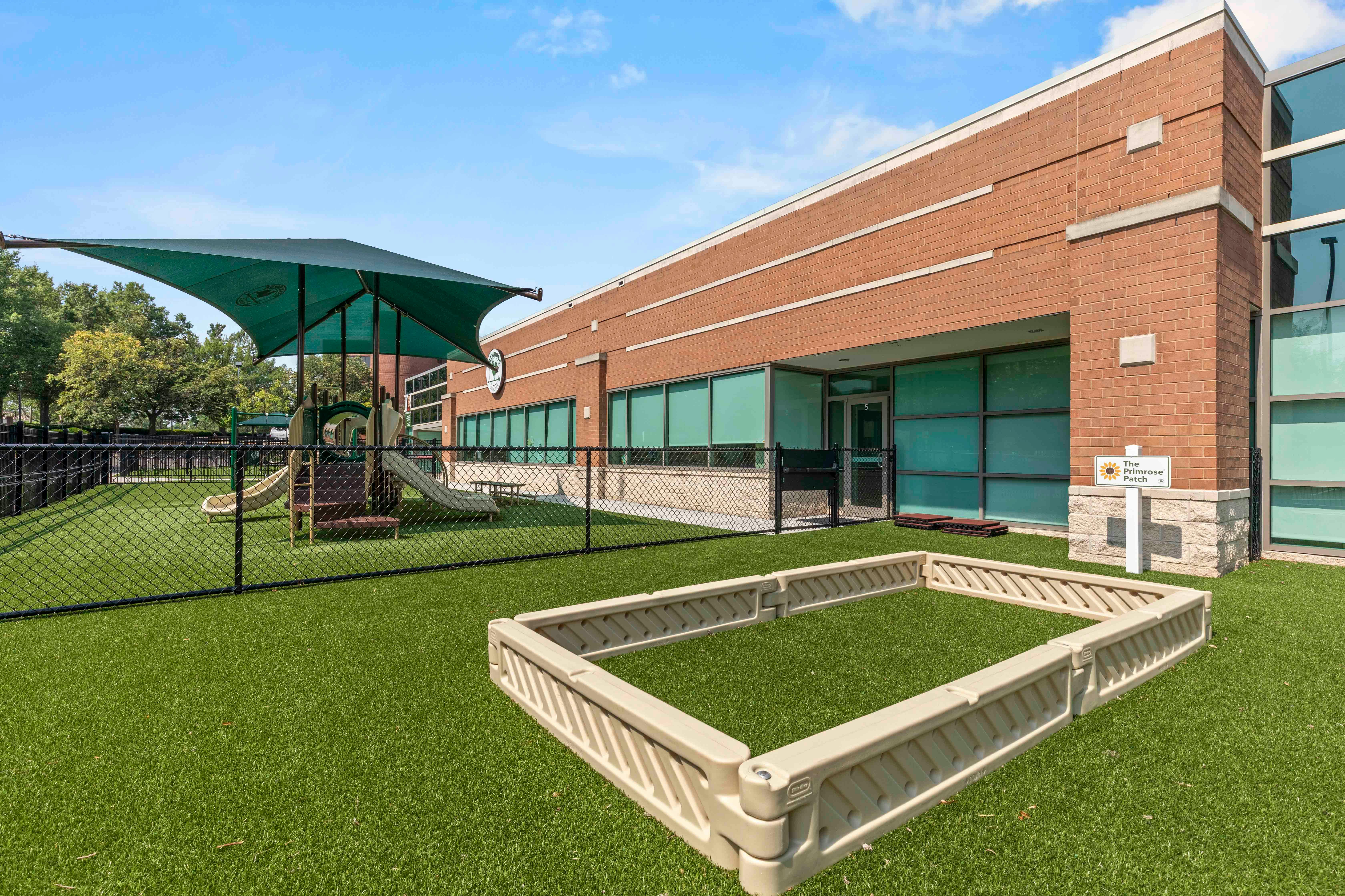 Playground with green turf, equipment with a shade, and a brick building