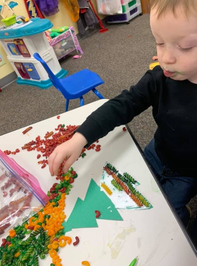 Child creating art with colored pasta on a table
