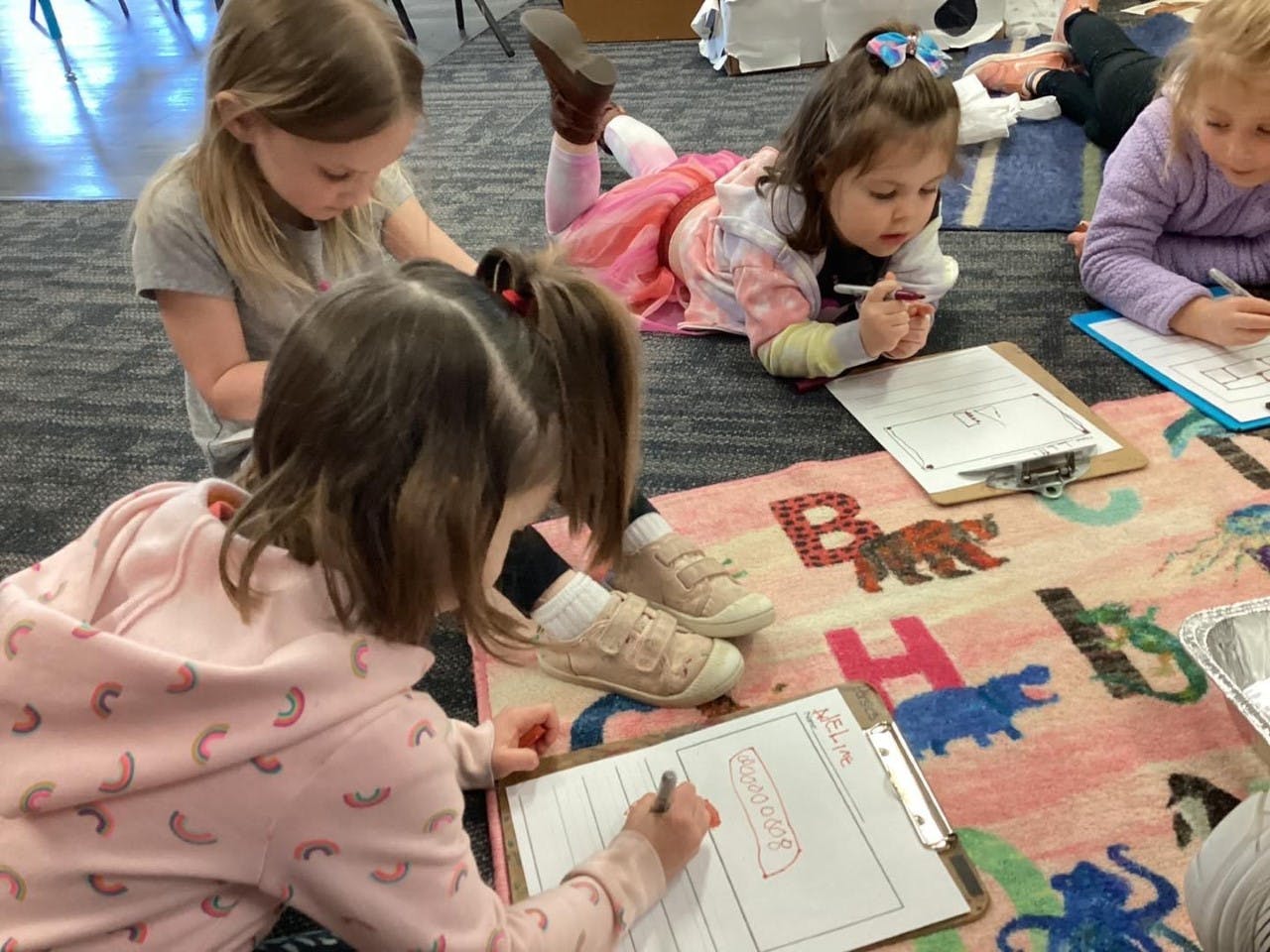 Children drawing on clipboards on a rug