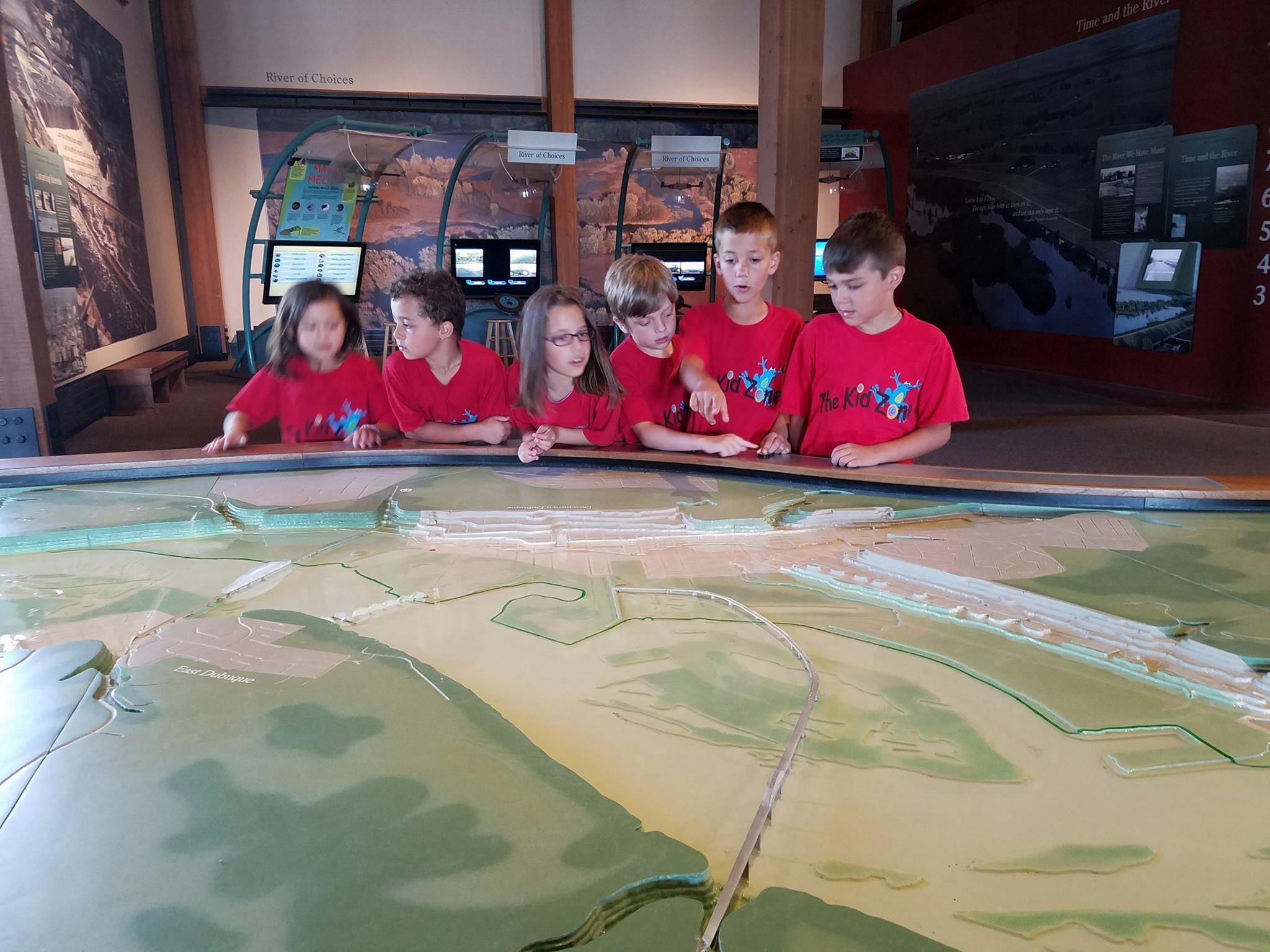 Children in red shirts looking at a large topographical map