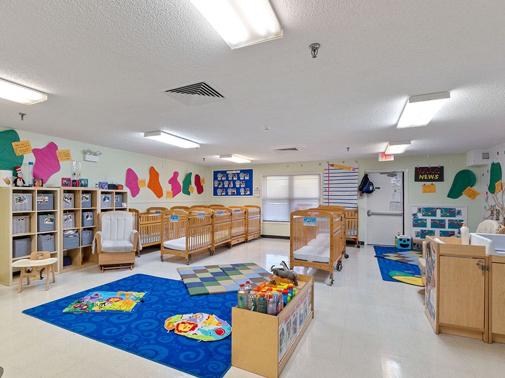 A colorful empty nursery room with multiple cribs, a rocking chair, and play mats