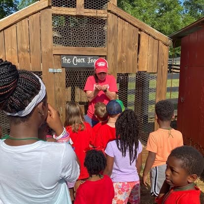 Person showing something to children in front of a chicken coop