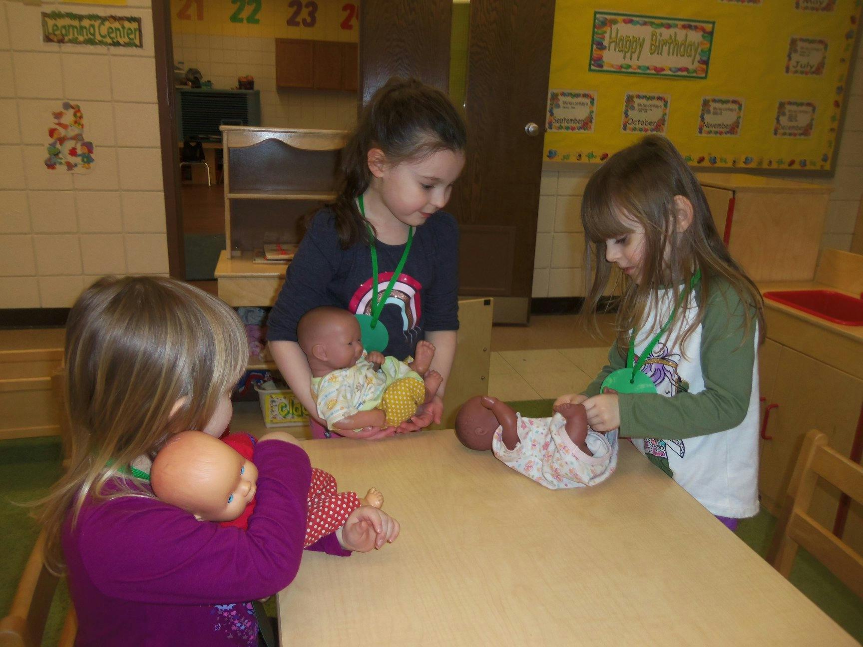 Three children playing with baby dolls in a classroom