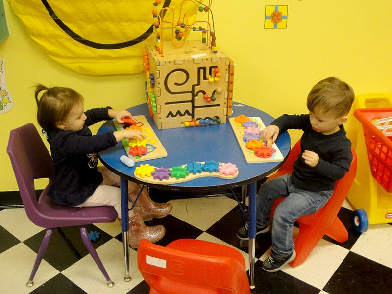 Two children playing with toys at a small table in a classroom