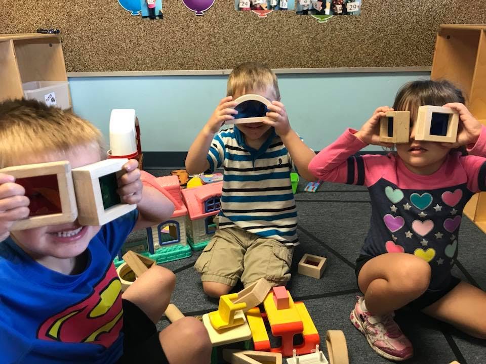 Three children playing with wooden blocks, holding them up to their eyes