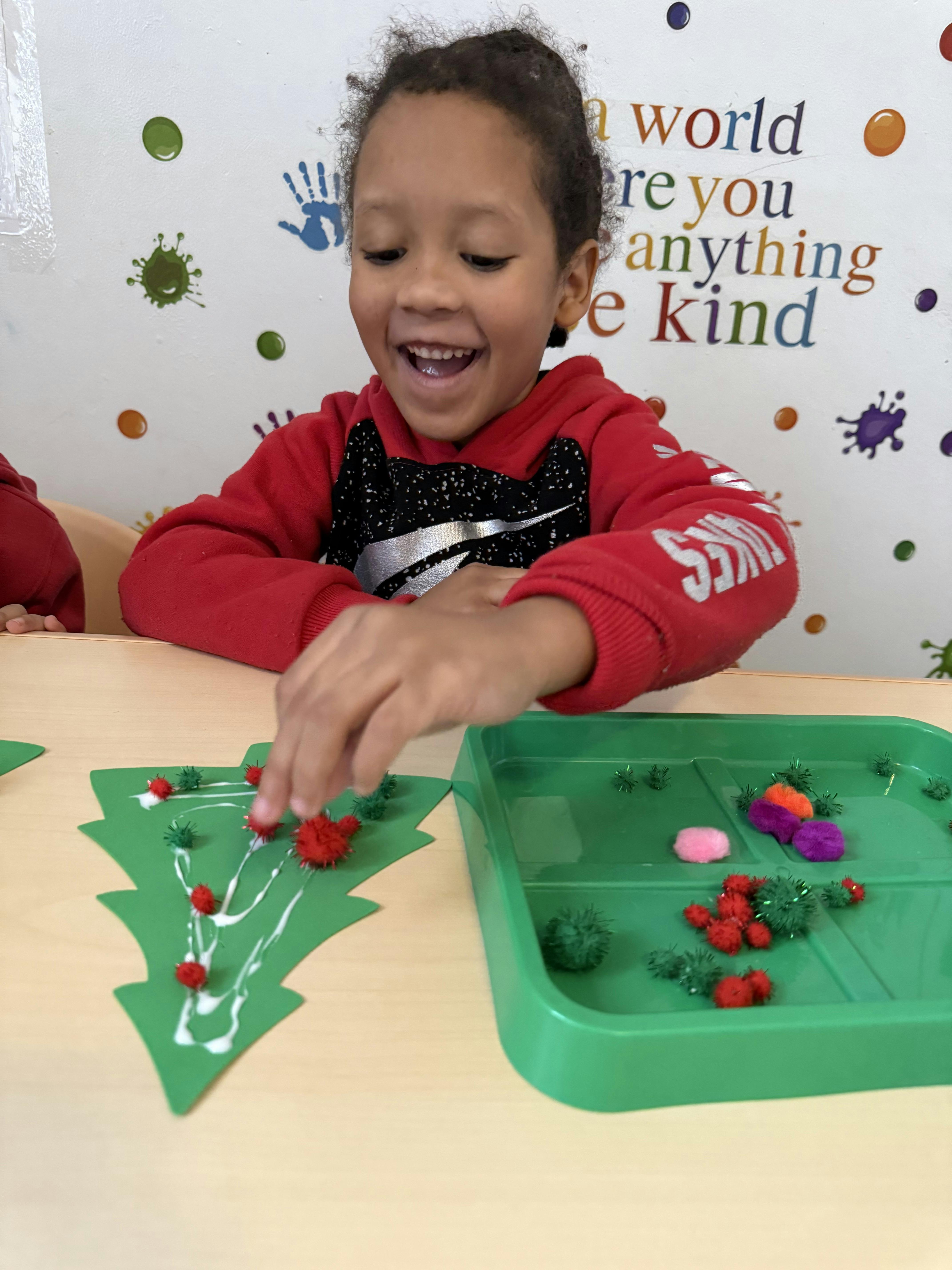 Child crafting with a paper tree and small pom-poms in a classroom
