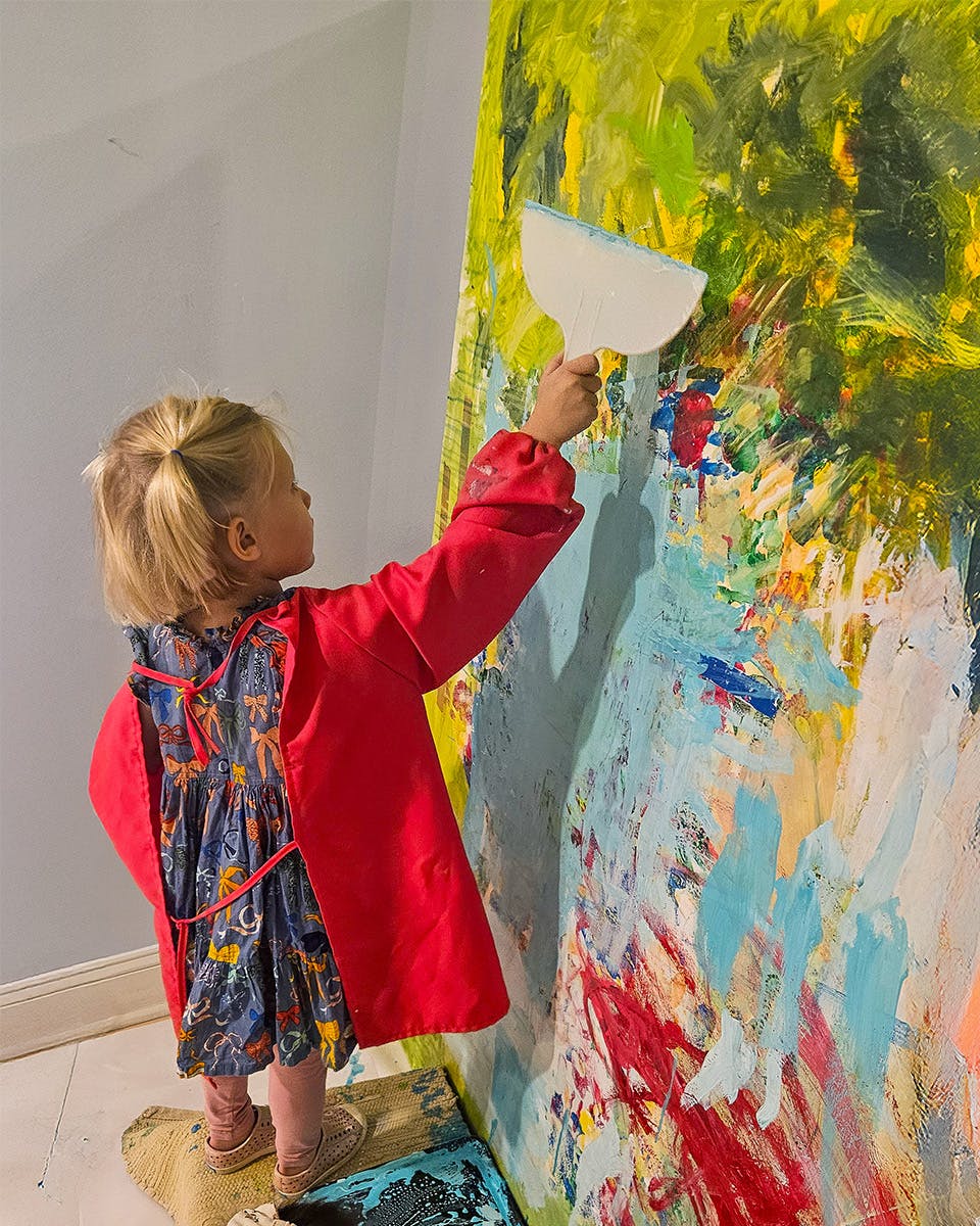 Child in a red smock painting a large canvas with a spatula