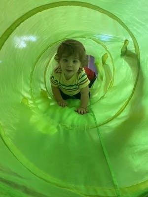 Child crawling through a green play tunnel