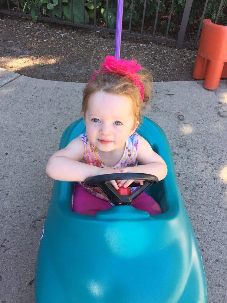 Child in a teal toy car with hands on the steering wheel