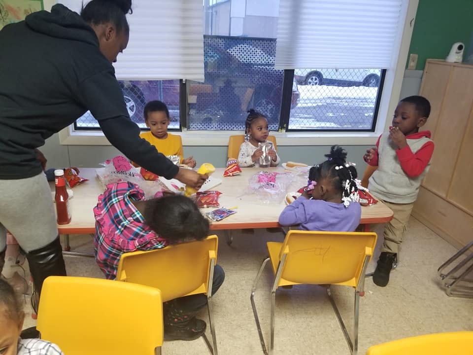 Person serving food to children at a table in a classroom