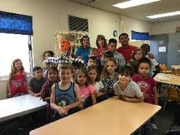 Group of children and adults posing with a scarecrow in a classroom