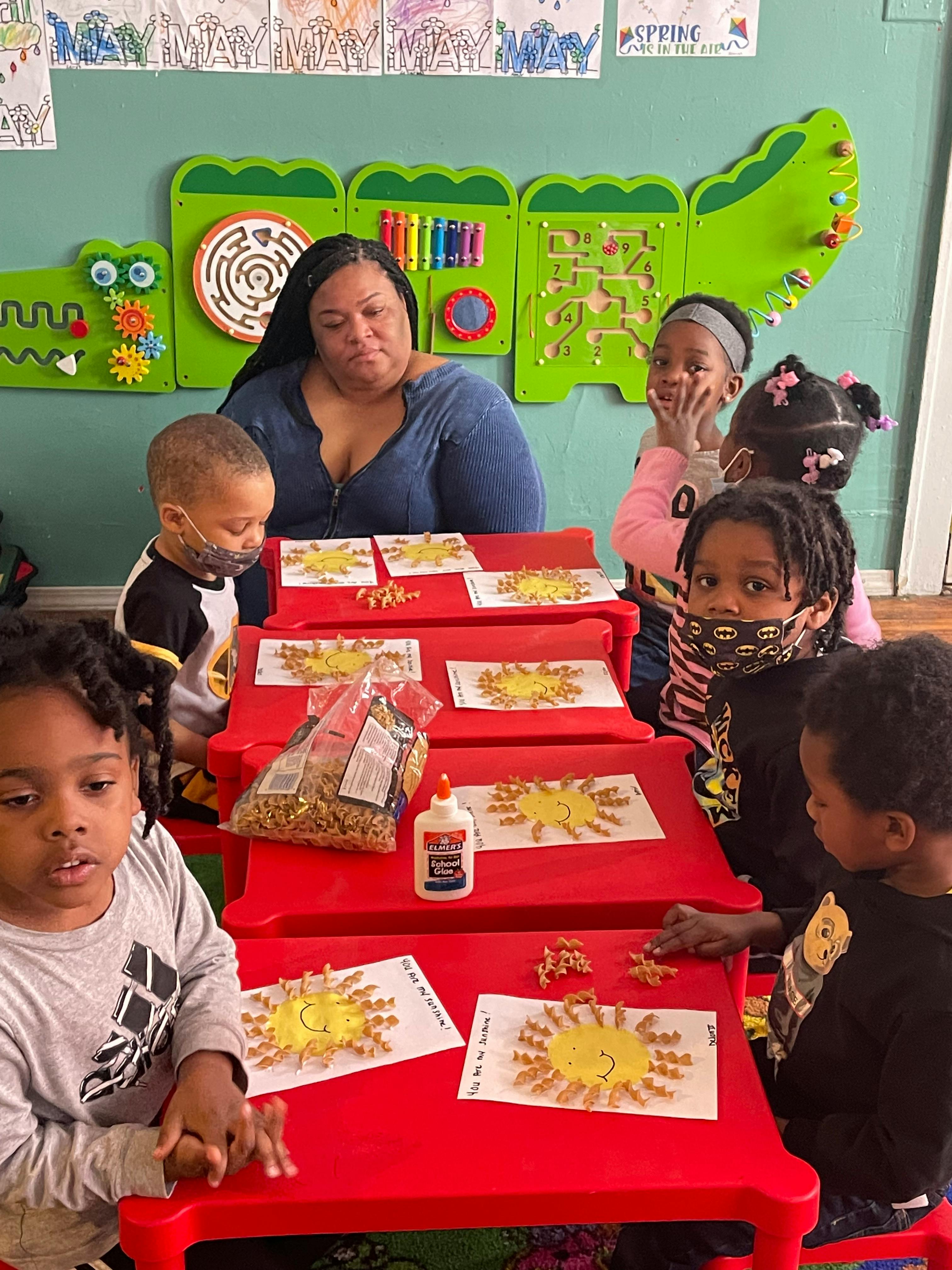 Adult and children at red tables doing a craft with pasta and glue