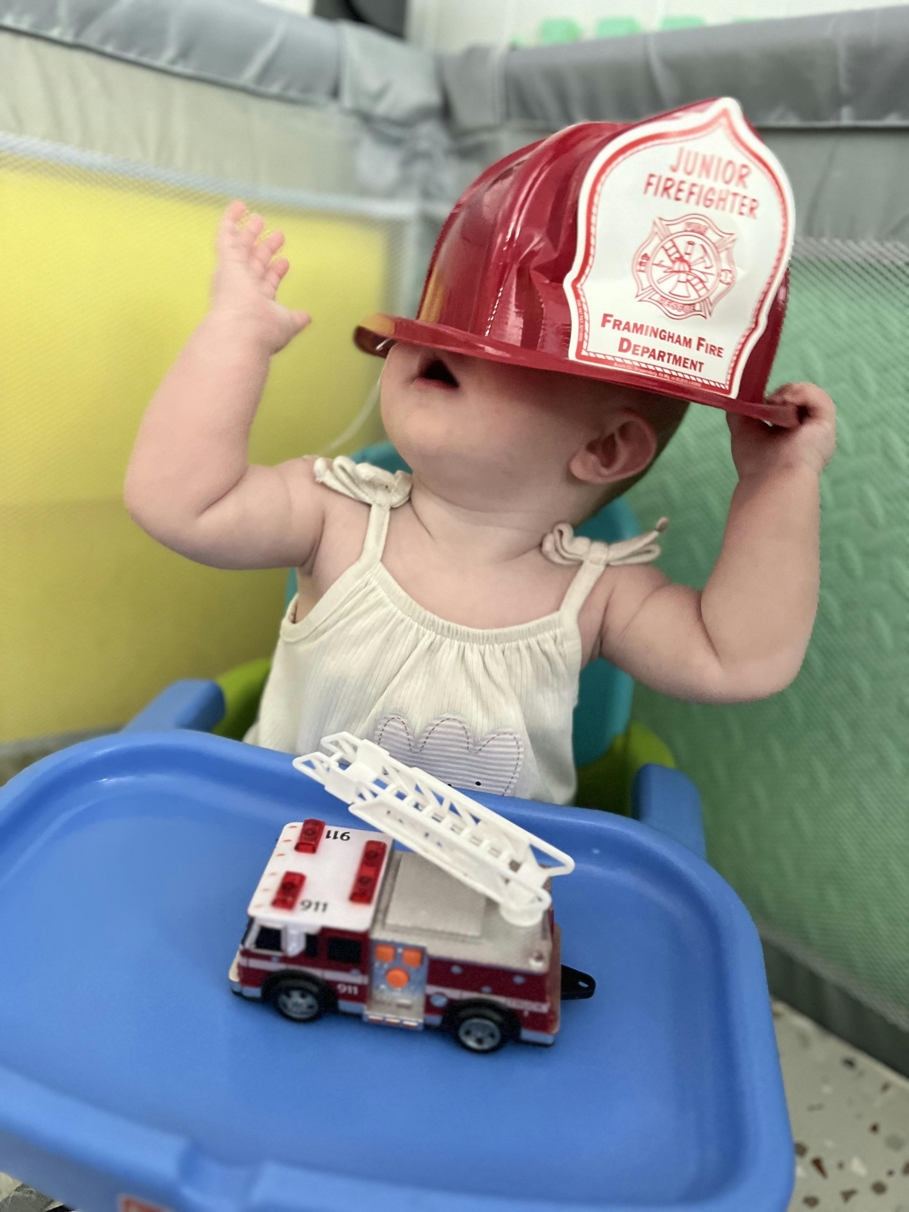 Child wearing a Junior Firefighter helmet with a toy fire truck on a tray