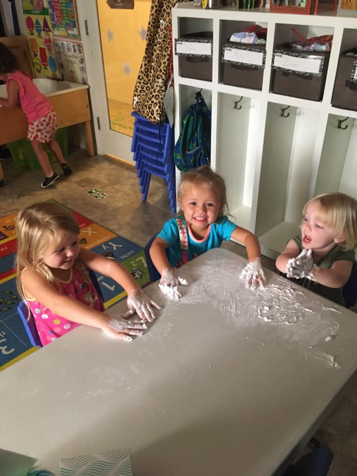 Three children playing with a white substance on a table
