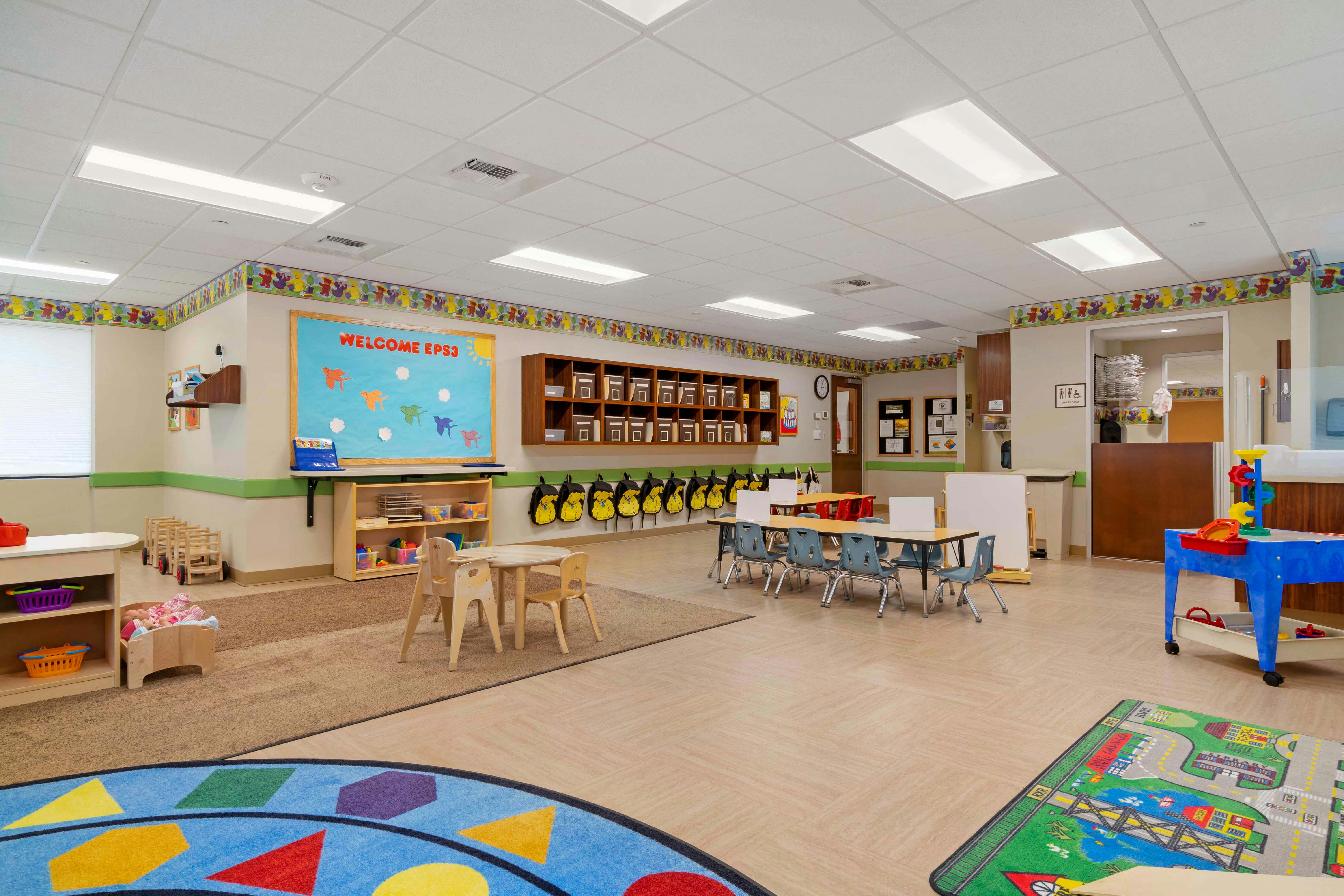 A classroom with a welcome board, children's tables and chairs, and play areas