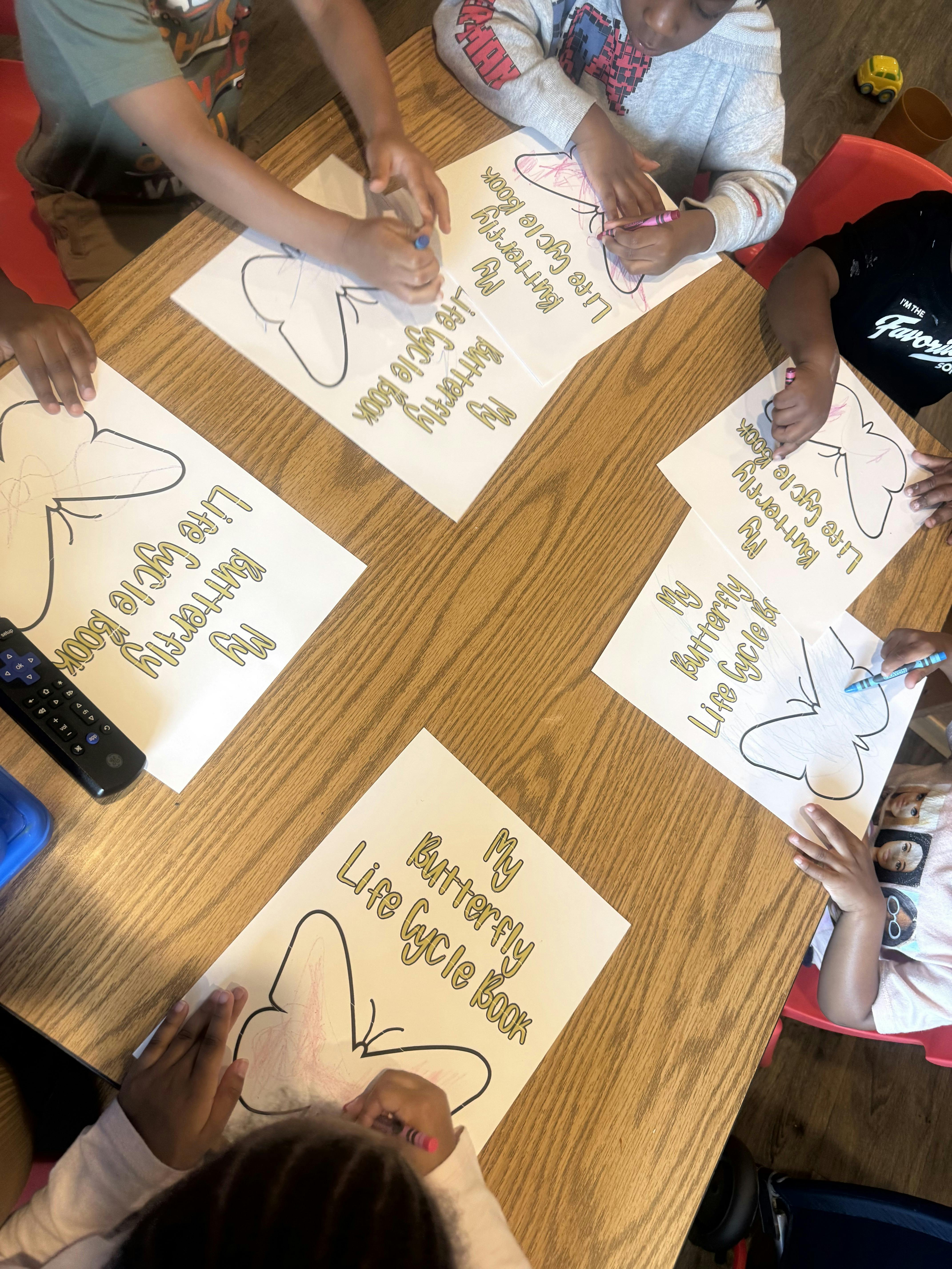 Children sitting at a table coloring butterfly life cycle books