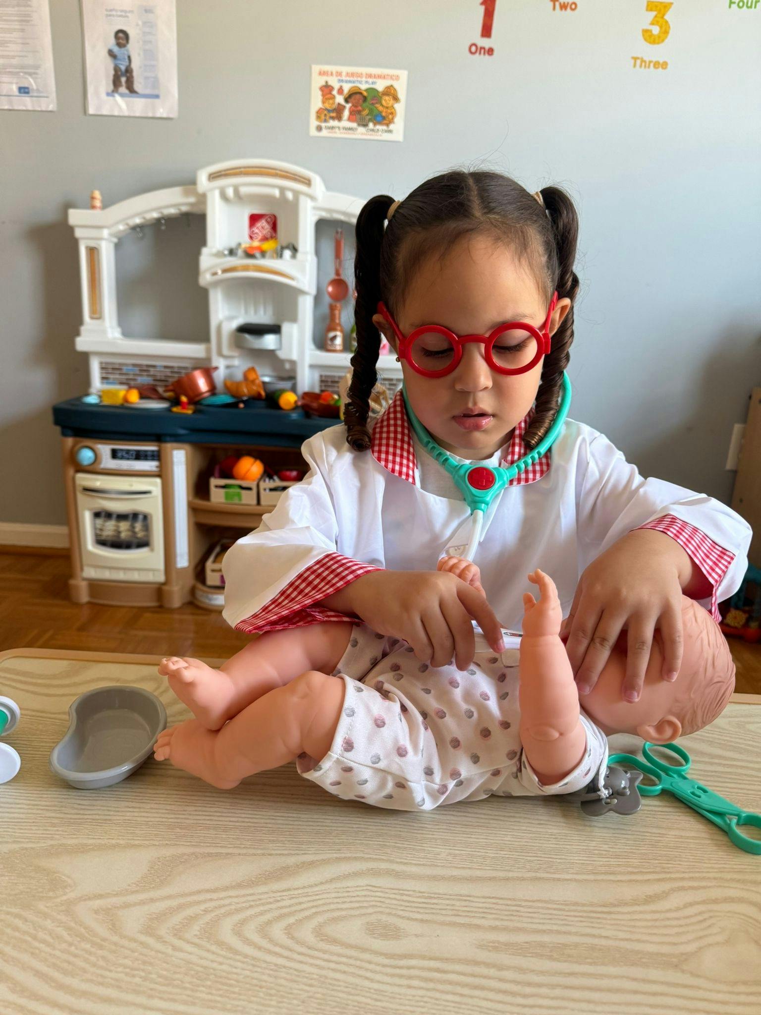 Child in doctor costume with stethoscope playing with a doll