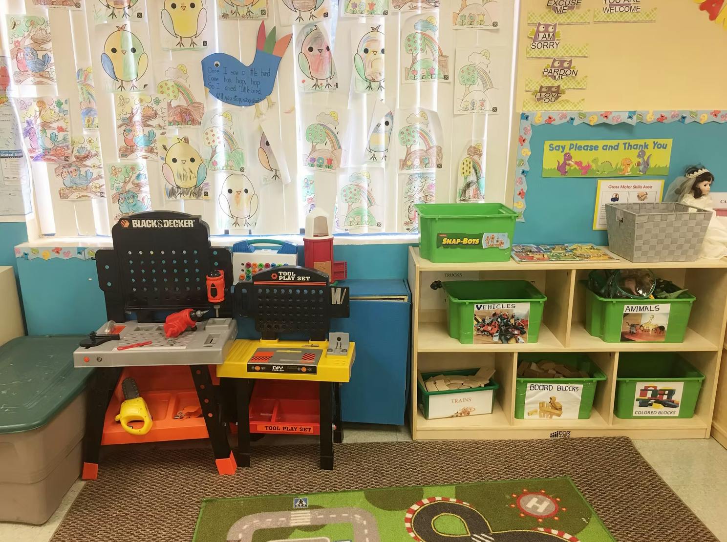 Play area in a classroom with a toy workbench and shelves with shelves of green bins