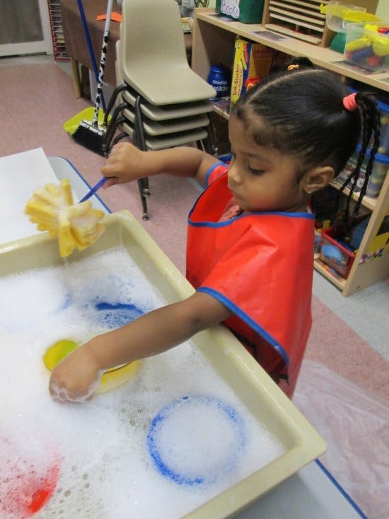 Child in a red smock playing with bubbles in a tray