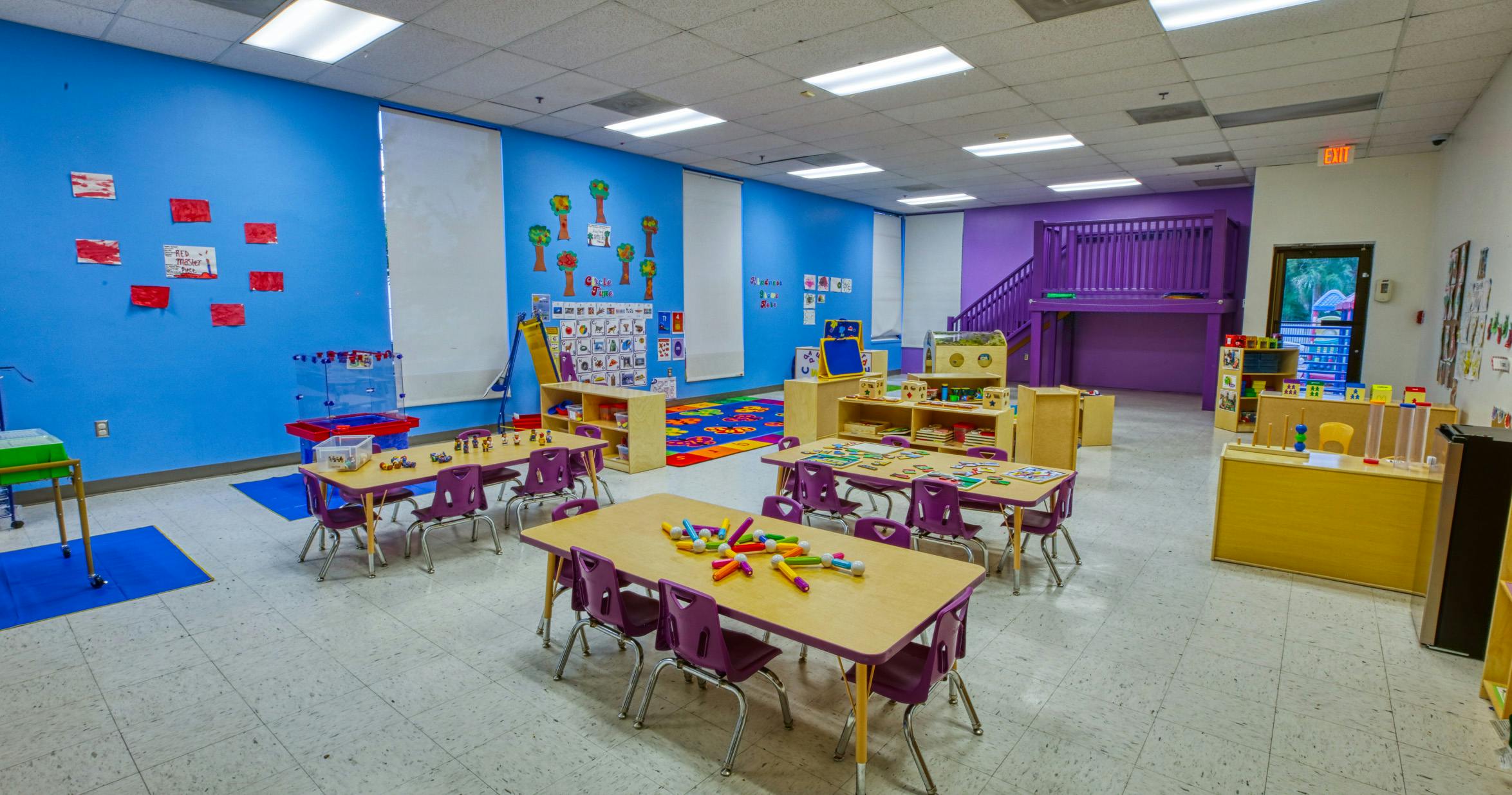 Classroom with small tables and chairs, toys, and educational posters on blue walls