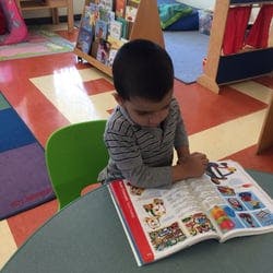 Child sitting at a table looking at a book