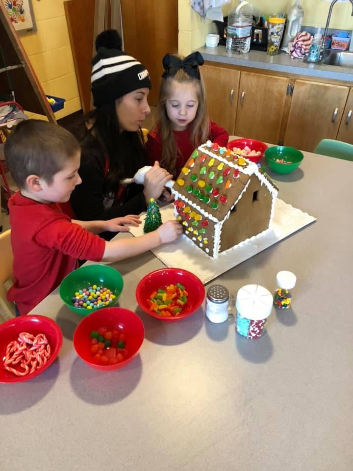 Adult and two children decorating a gingerbread house