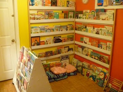 Children's books displayed on wall shelves and a floor rack with cushions