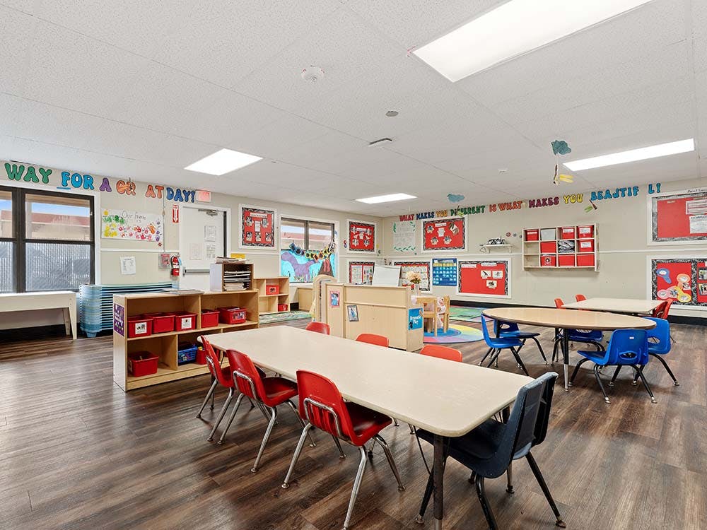 Classroom with child-sized tables and chairs, shelves, and decorations on walls