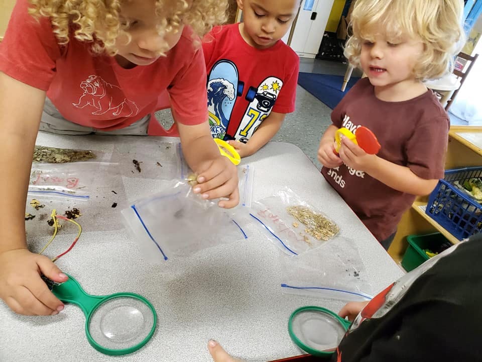 Children examining items in plastic bags with magnifying glasses