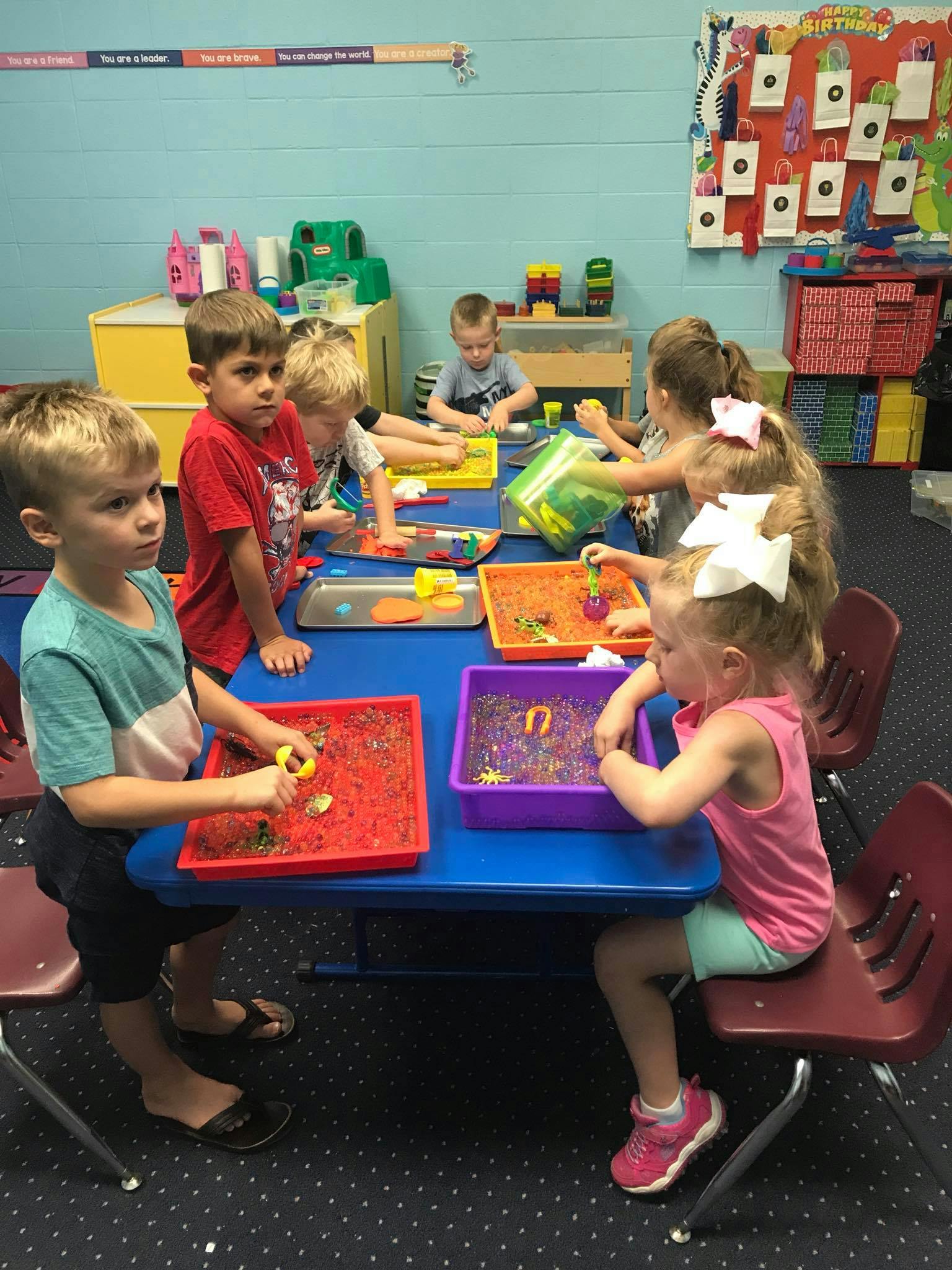 Children playing with sensory bins at a table in a classroom