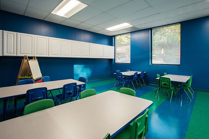 Classroom with blue walls, white cabinets, and tables with blue and green chairs