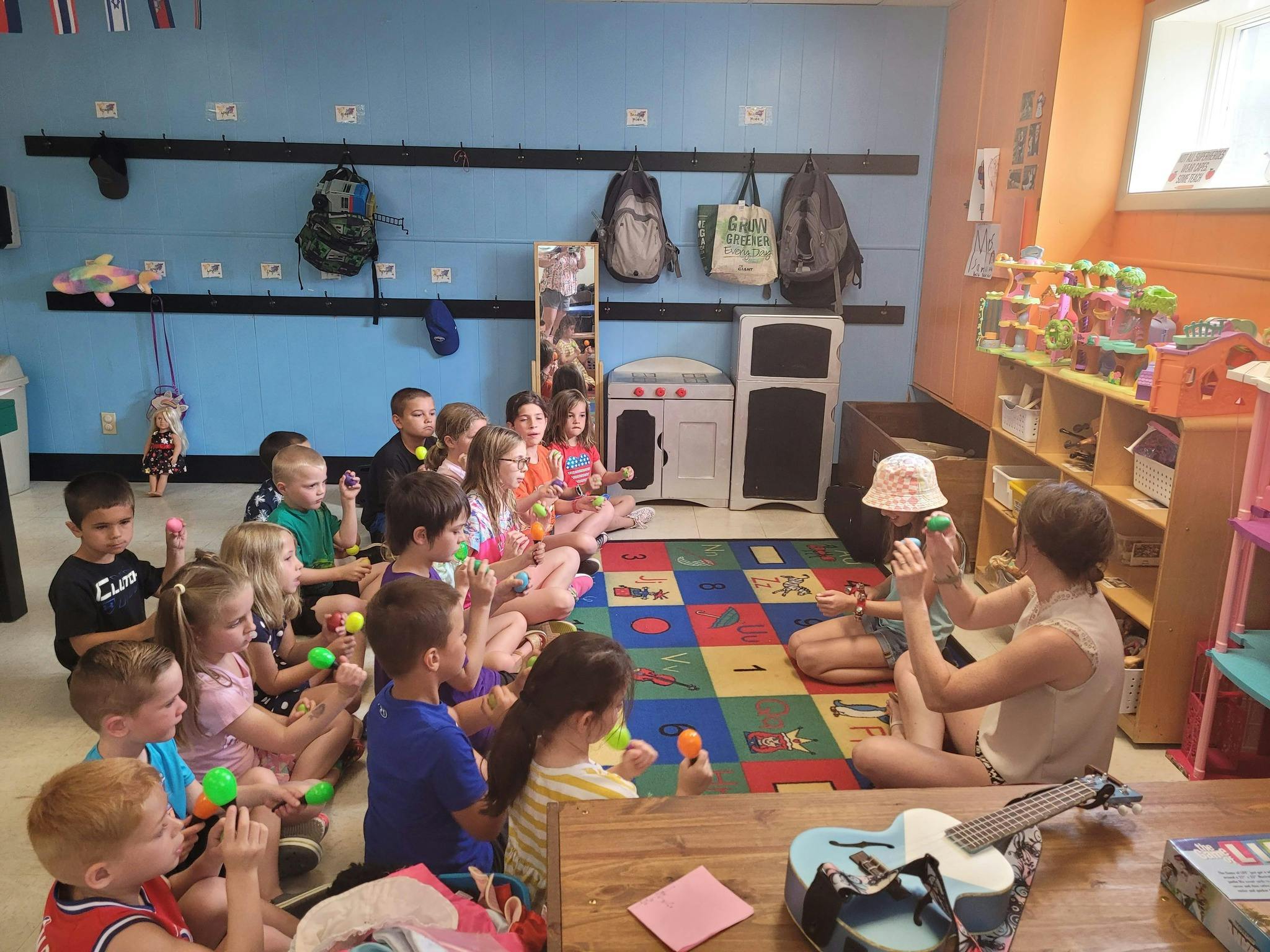 Children sitting on a colorful rug in a classroom, holding shakers