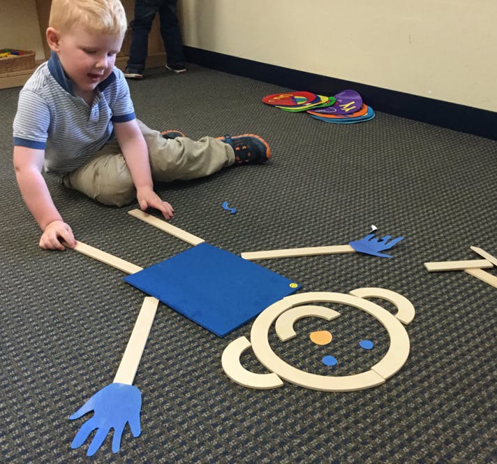 Child on floor playing with wooden and blue cutouts