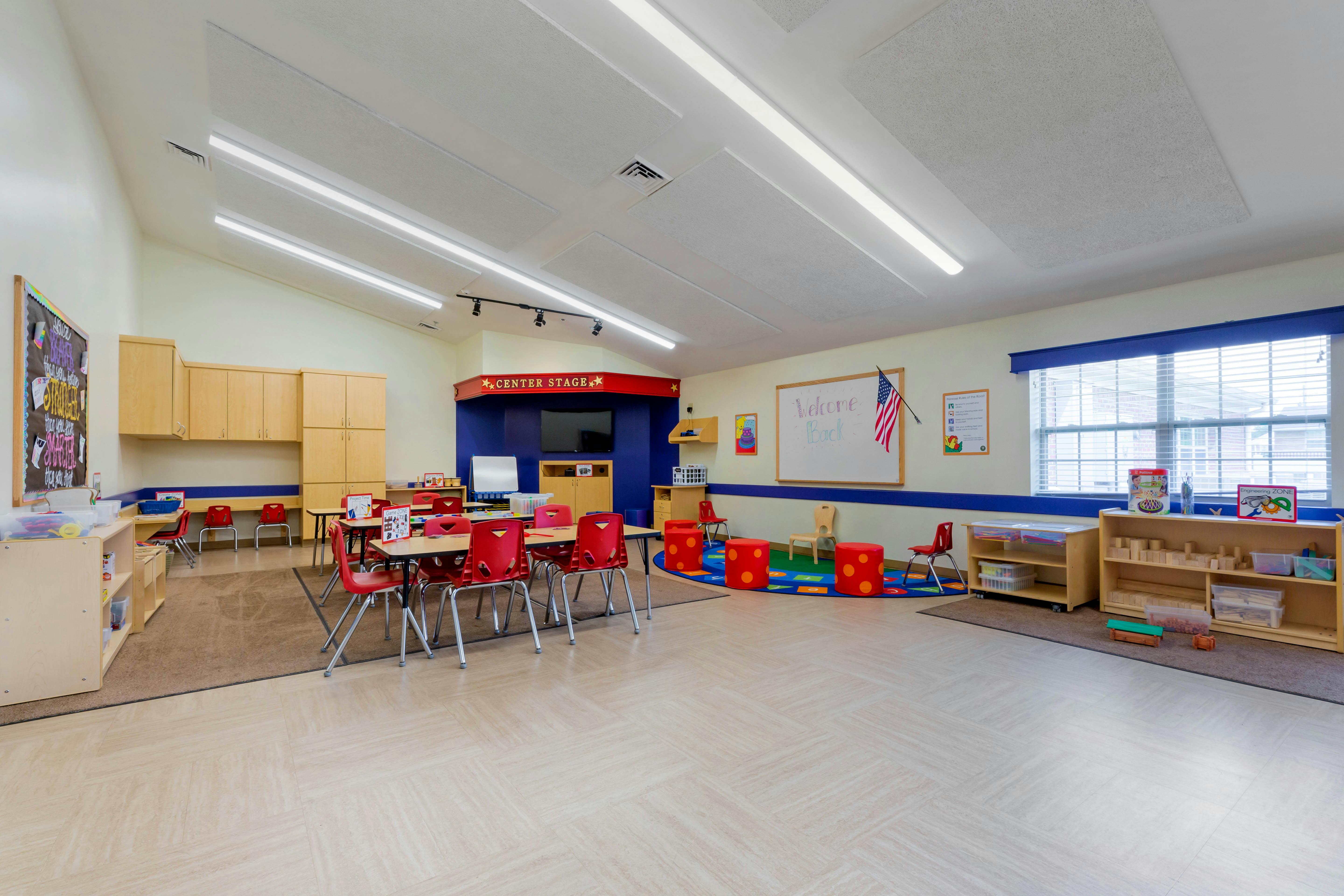 Classroom with small red chairs and tables, a “Welcome Back” whiteboard, and cubbies