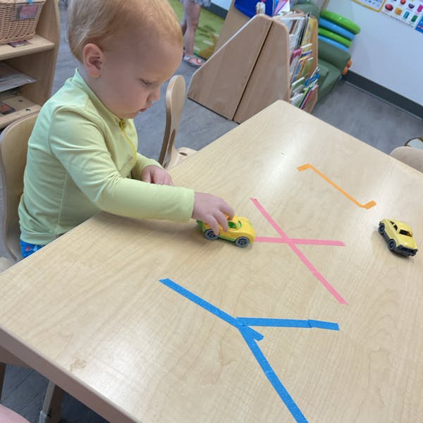 Child playing with toy cars on a table with tape lines