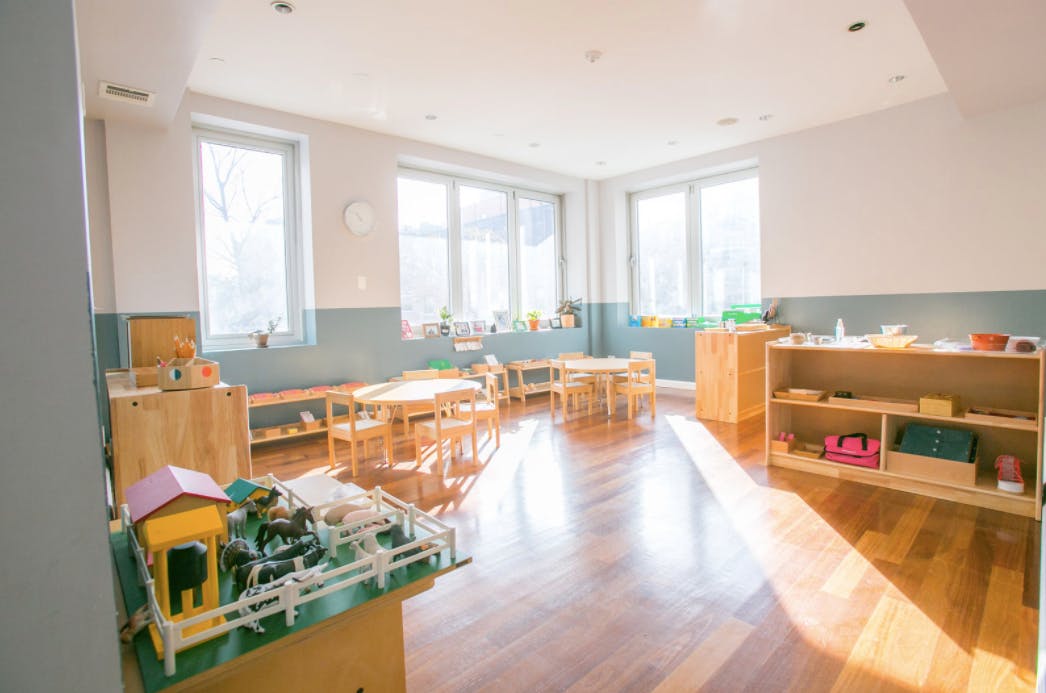 Empty classroom with small tables and chairs, shelves with toys