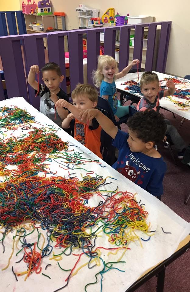 Children playing with colorful strings at a table in a classroom