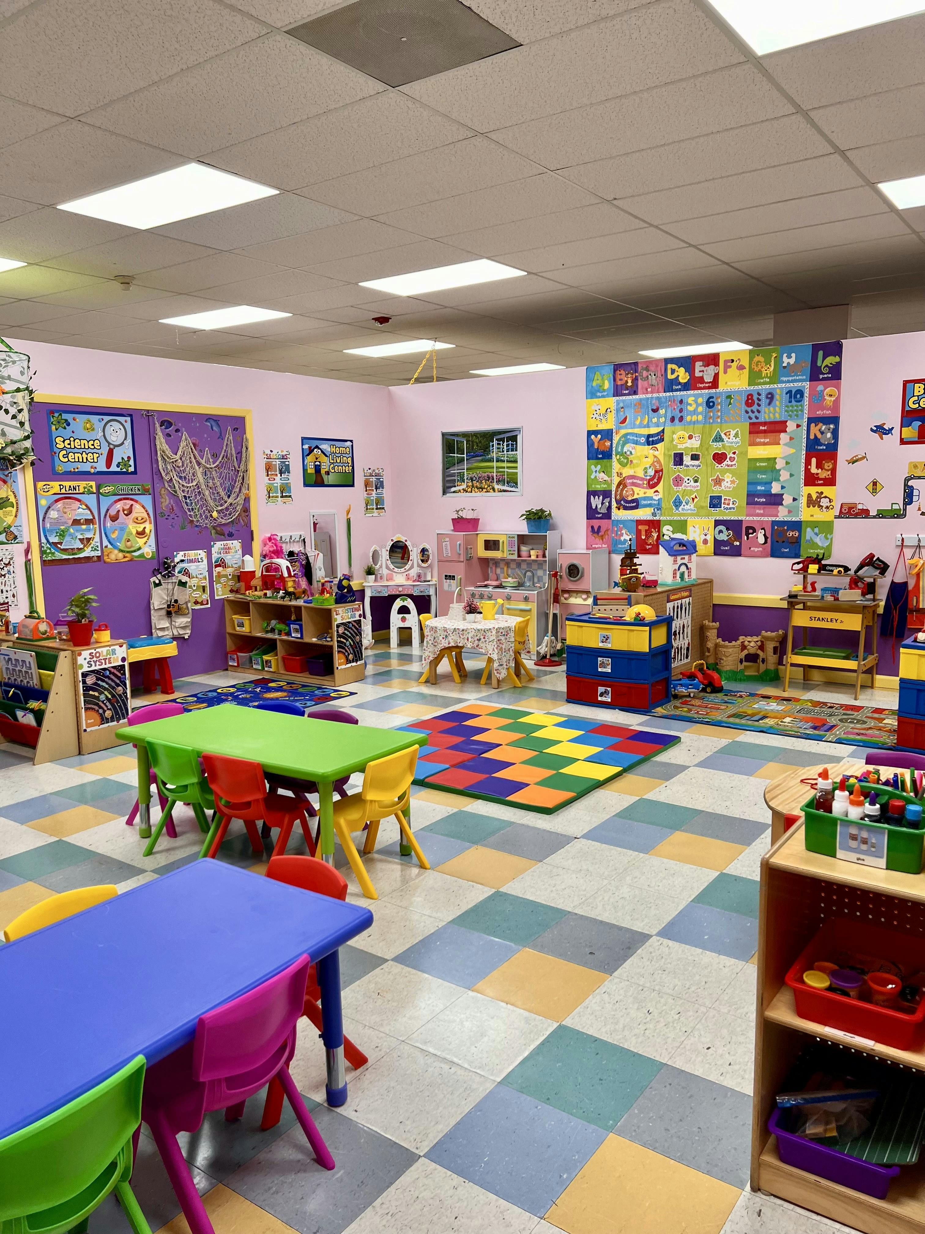 Colorful classroom with small tables and chairs, play areas, and educational posters