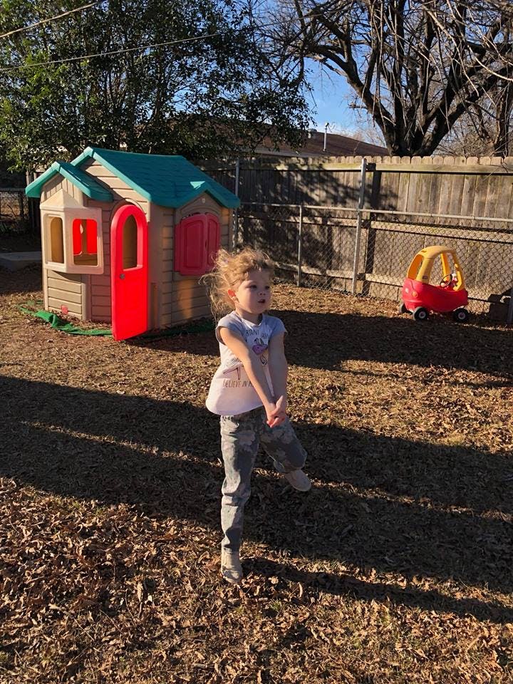 Child standing in a yard with a playhouse and toy car
