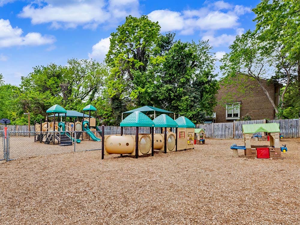 A fenced playground with various play structures and wood chips on the ground